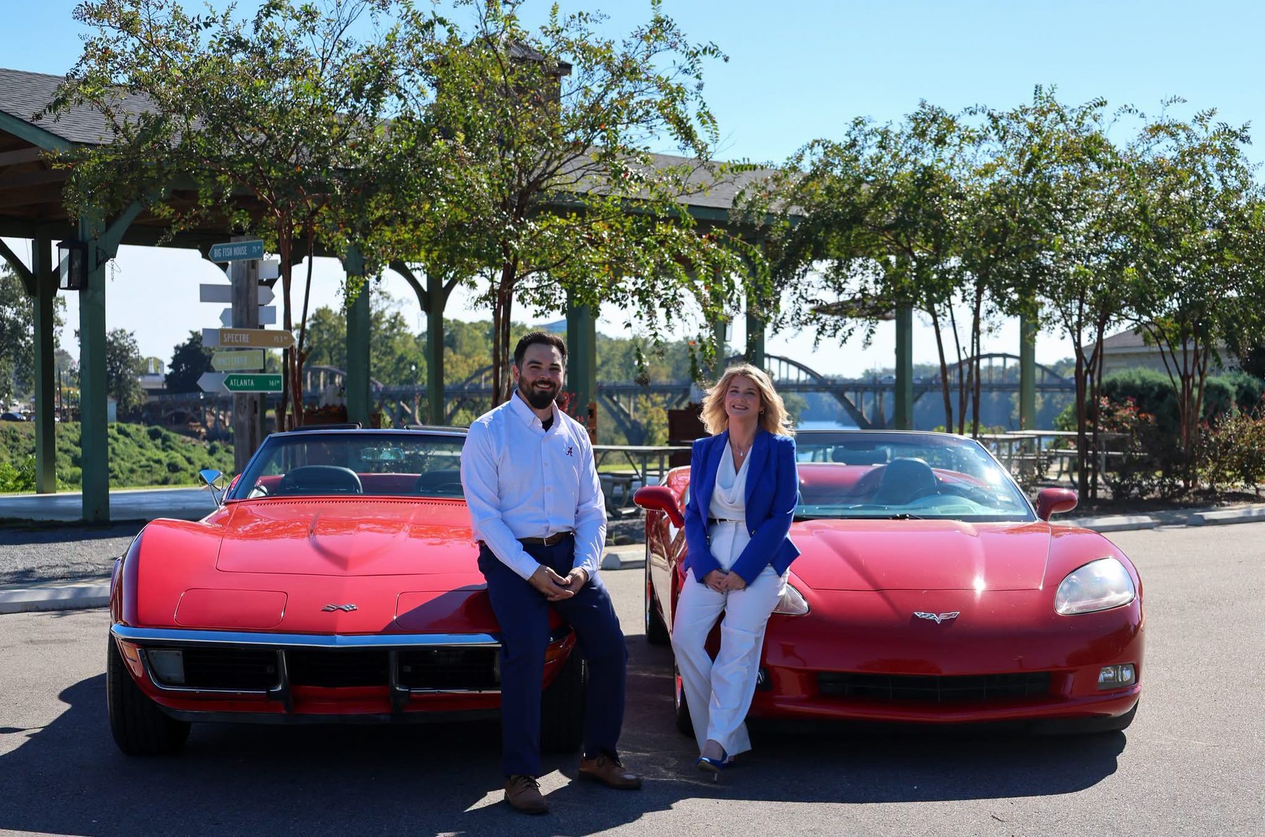 Chris and Courtney Lowry sitting on their two red Corvettes by the Coosa River in downtown Wetumpka